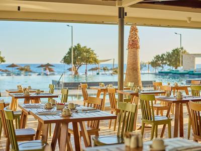 Open restaurant with wooden tables and sea view in sunshine.