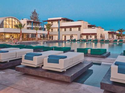 Modern hotel complex with pool, sunbeds, and palm trees under clear sky.