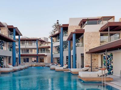 Modern hotel complex with multi-story buildings and large outdoor pool under blue sky.