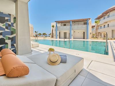 Modern pool area with loungers, sunshade, and adjacent buildings under clear sky.