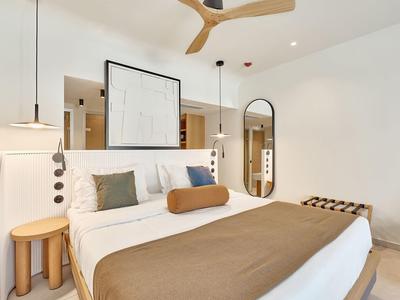 Modern hotel room with large bed, decorative pillows, and minimalist design.