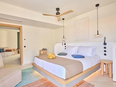 Bright, minimalist bedroom with large bed, ceiling fan, and view into an adjoining room.