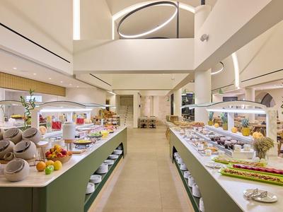 Modern breakfast buffet with diverse foods in a bright restaurant with high ceiling.