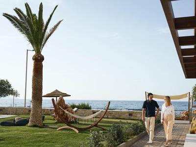 Paar geht am Hotelgarten mit Palmen und Hängematte zum Meer entlang.