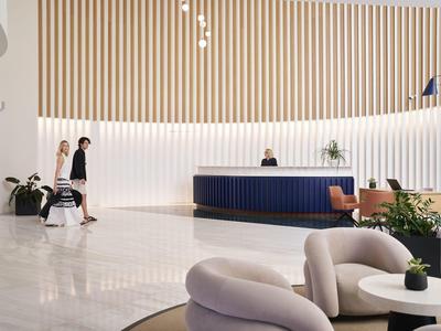 Modern hotel lobby with light flooring, blue reception desk, and seating areas.