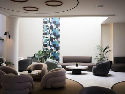 Modern furnished waiting area with cozy armchairs and plants in a bright room.