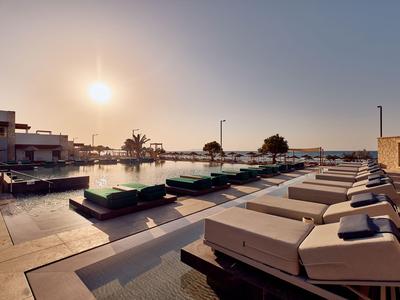 Zonnig zwembadgebied met ligstoelen en uitzicht op moderne gebouwen aan het water.