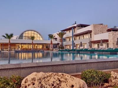 Modern hotelcomplex met groot zwembad en parasols bij heldere lucht.