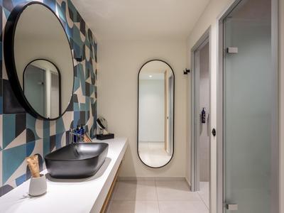 Bagno moderno in hotel con specchi ovali, superfici bianche e piastrelle con motivo geometrico.