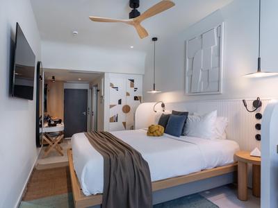 Camera d'hotel moderna con letto grande, ventilatore a soffitto e arredamento minimalista.
