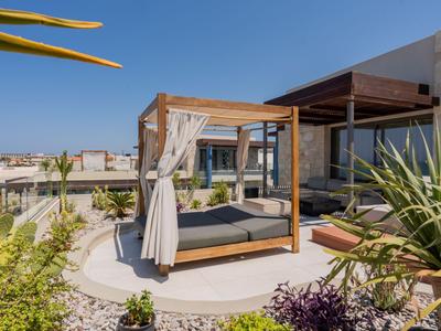 Lounge moderna con lettino e tende su terrazza con vista su edifici bianchi.