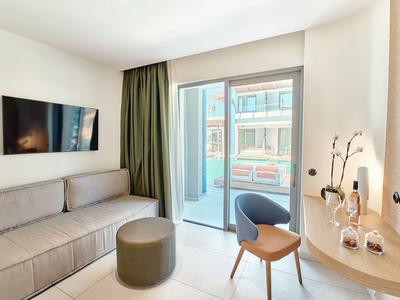 Camera d'hotel moderna con divano ad angolo, piccolo tavolo e balcone con vista esterna.
