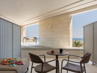 Balcone moderno con tavolo e sedie, vista mare e lettino bianco.