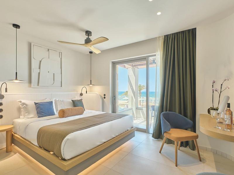 Modern hotel room with double bed, balcony access with sea view, bright and minimalist decor.
