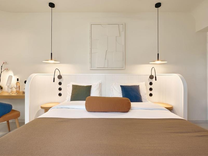 Modern hotel room with double bed, brown bedspread, and stylish white wall lamps.