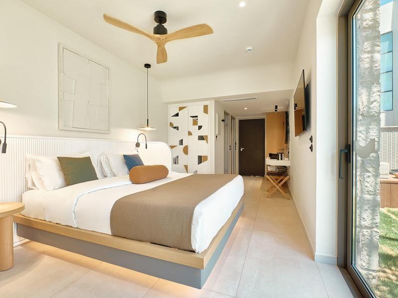 Modern hotel room with double bed, ceiling fan, and balcony access overlooking outdoors.