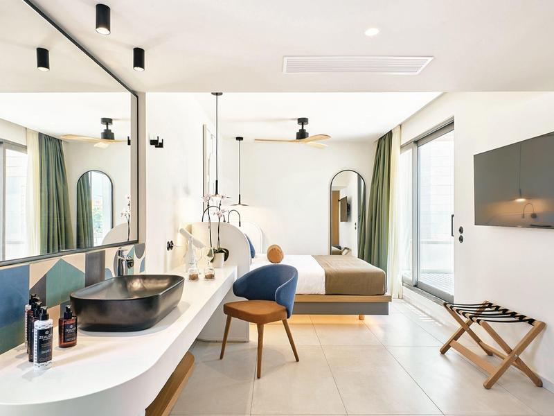 Modern hotel room with double bed, desk, chair, and large mirror.