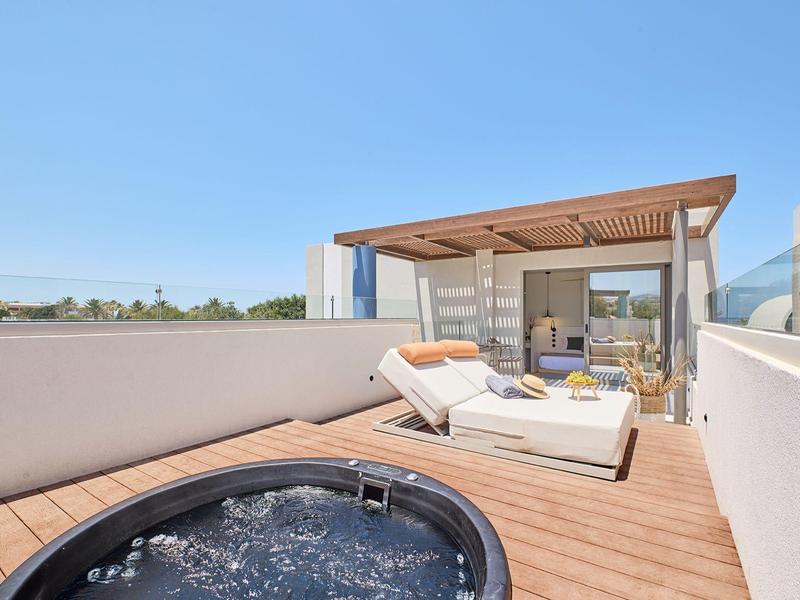 Terrace with jacuzzi, sun loungers, and covered seating area under clear sky.