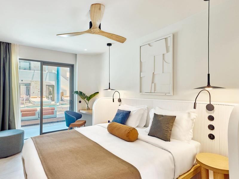 Modern hotel room with large bed, ceiling fan, and balcony overlooking city view.