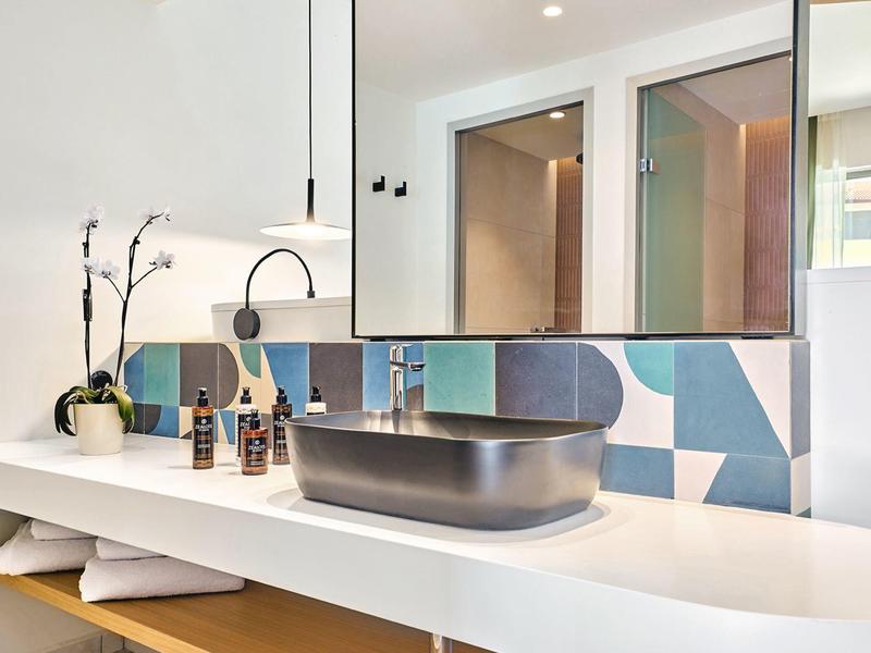 Modern bathroom with white vanity, gray basin, and colorful tiled backsplash.