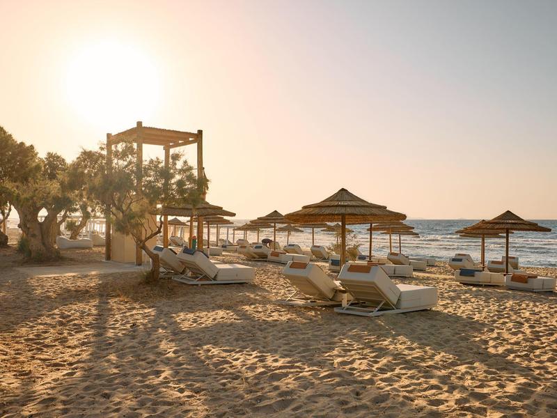 Beach with sun loungers and straw umbrellas at sunset by the sea
