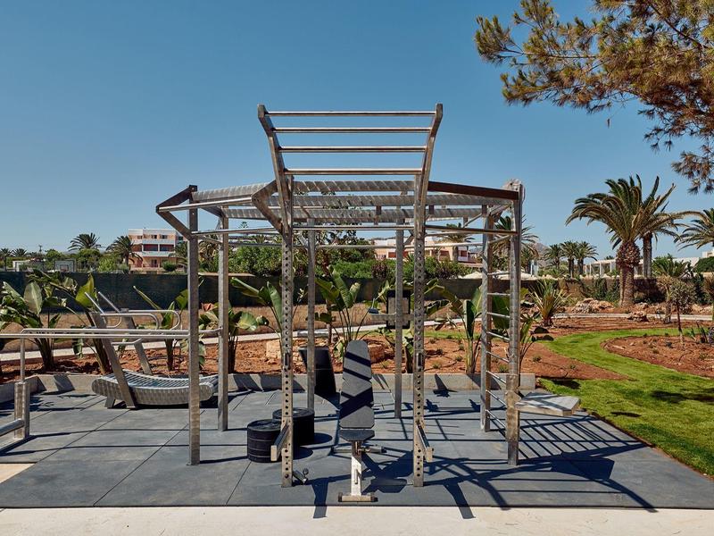 Outdoor area with swings and climbing frame in a sunny garden near a hotel.