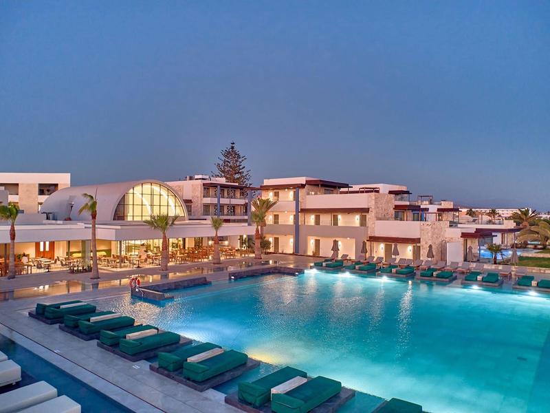 Illuminated hotel pool with loungers and modern architecture at dusk.