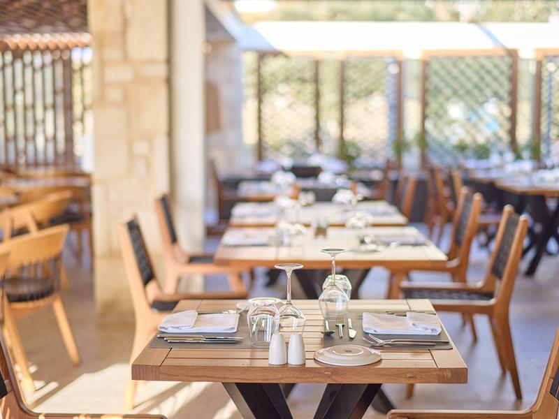 Elegant outdoor restaurant with wooden tables and chairs set with plates and glasses.