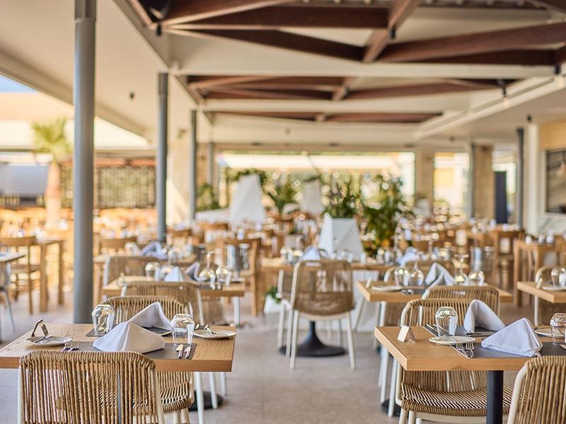 Spacious, bright restaurant with wooden chairs, set tables, and modern wooden beams on the ceiling.