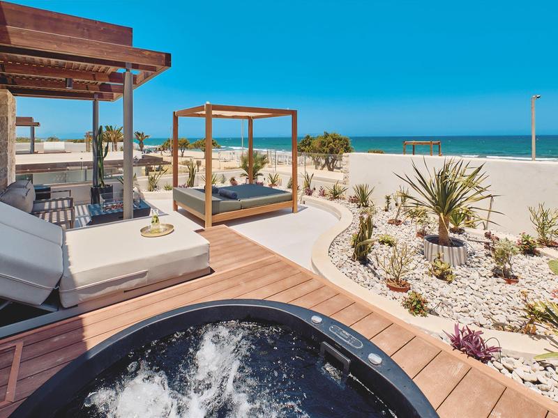 Luxury terrace with hot tub, sun loungers, and view of sandy beach and sea.