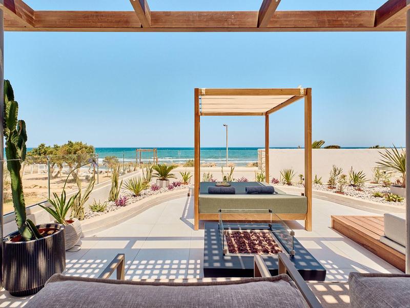 Modern beach pavilion with pergola, seating area, and sea view under clear sky.