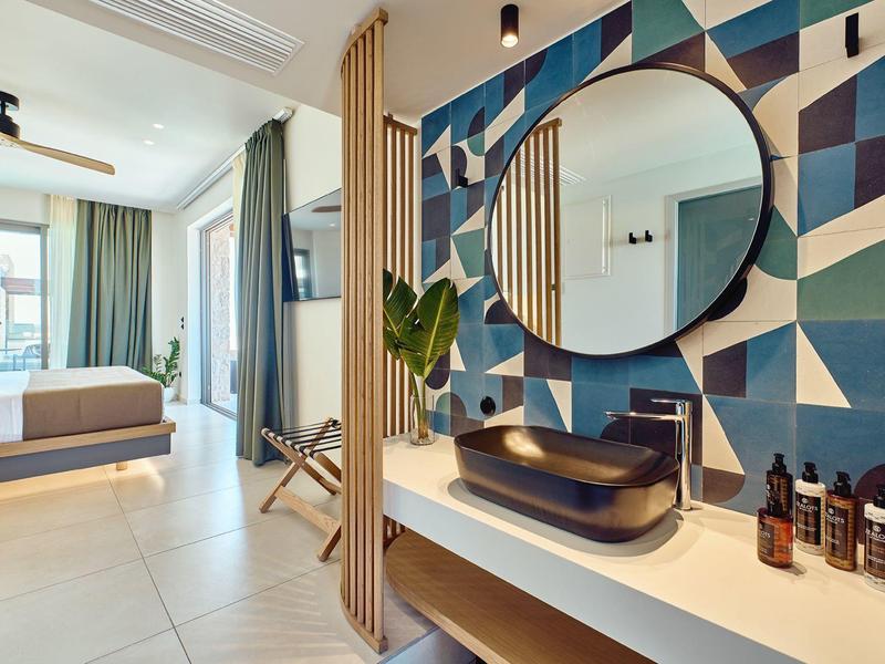 Modern hotel room with open bathroom, geometric wall design, and large windows.