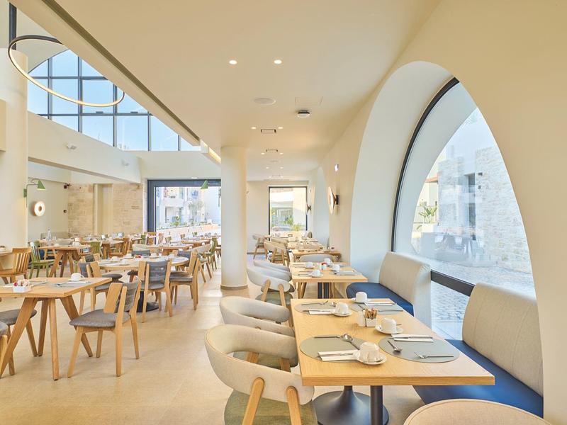 Bright restaurant area with large round windows and modern wooden furniture.