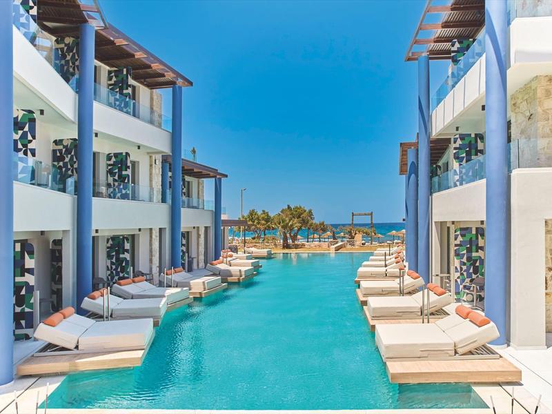 Modern hotel pool with loungers between two multi-story buildings under clear blue sky.