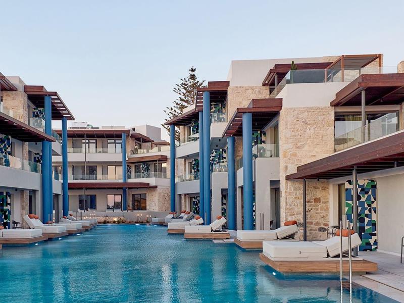 Modern hotel complex with multi-story buildings and large outdoor pool under blue sky.