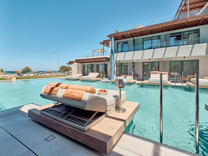 Modern hotel with pool, loungers, and terrace view under sunny skies.