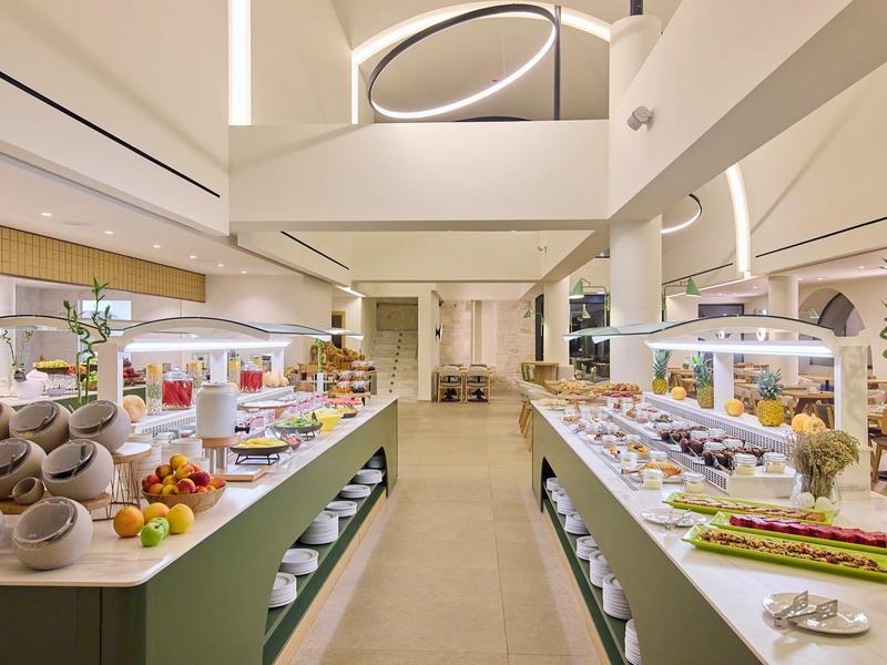 Modern breakfast buffet with diverse foods in a bright restaurant with high ceiling.