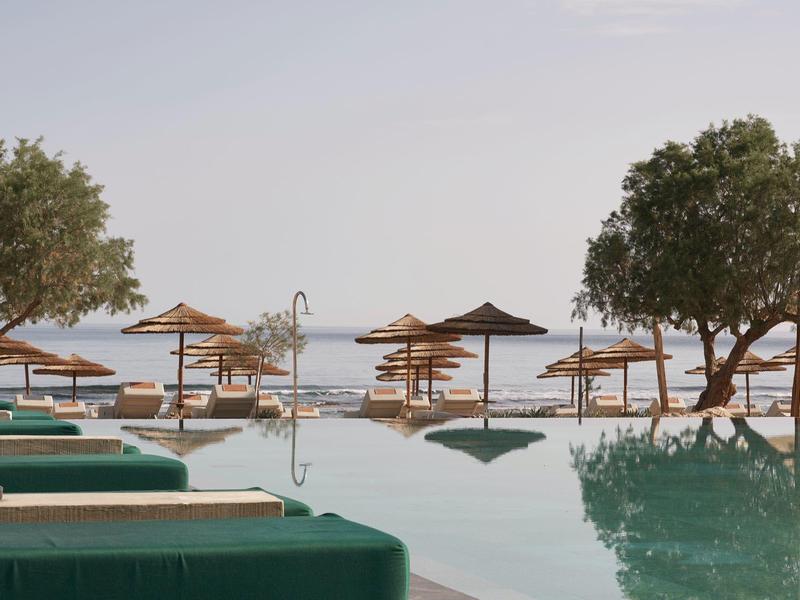 Infinity pool with loungers and umbrellas overlooking calm sea and trees