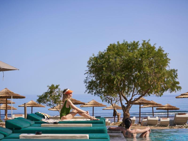 Woman in green swimsuit relaxing by the pool with palm trees and sun umbrellas in the background.