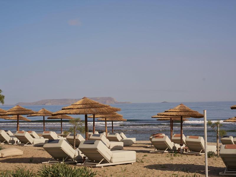 Empty sun loungers and thatched sun umbrellas on the beach overlooking the calm sea.