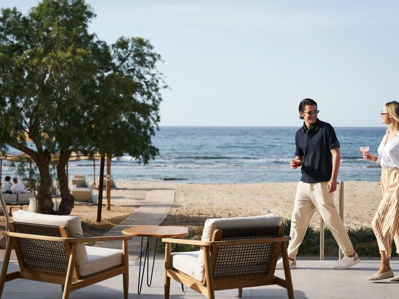 Two people walking along a beach with trees and chairs.