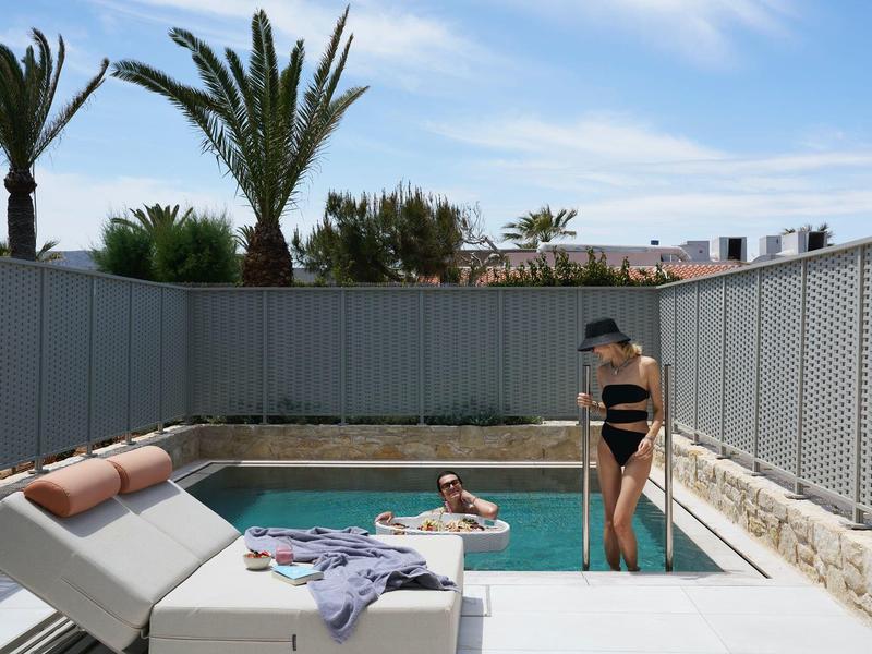 Woman steps into a small outdoor pool at a hotel on a sunny day.