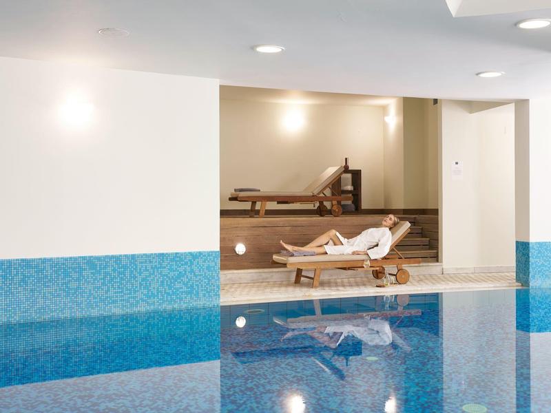 Indoor pool with blue tiles and lounge chair in a relaxation area.