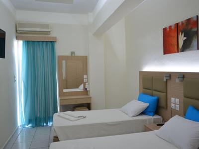 Habitación de hotel luminosa con dos camas individuales, ropa de cama azul y blanca y pequeño televisor en la pared.