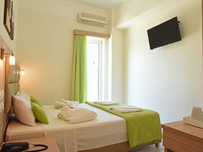 Habitación de hotel sencilla con cama, toques verdes y televisor de pared.