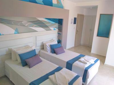 Habitación de hotel luminosa con dos camas individuales, paredes blancas y detalles en azul.
