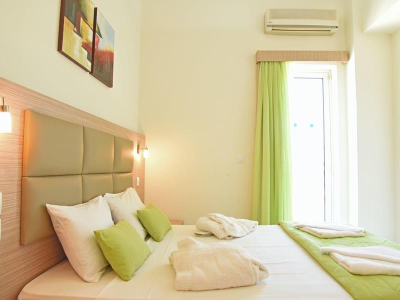 Habitación de hotel luminosa con cama doble, acentos verdes y luz natural a través de una ventana con cortina.