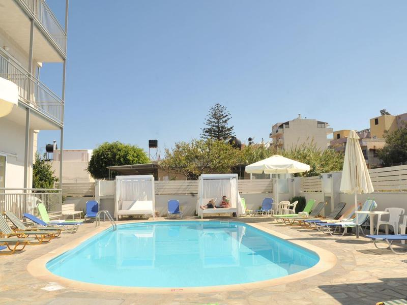 Piscina de hotel con tumbonas, sombrillas y cabañas bajo un cielo azul claro.