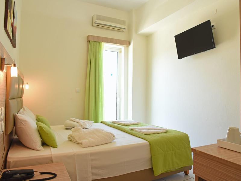 Habitación de hotel sencilla con cama, toques verdes y televisor de pared.