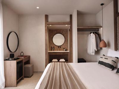 Modern hotelkamer met tweepersoonsbed, open kledingkast en uitzicht op badkamer.